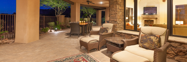 Photo of elegant patio with outdoor patio funiture complete with candles lit on a table. Big windows on the back of the house let you see into the well-lit living room with a fireplace.
