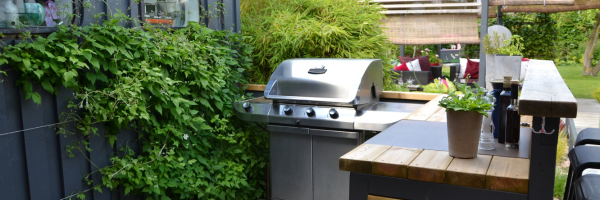 Outdoor kitchen with integrated BBQ Grill agains an outdoor fence with vines.