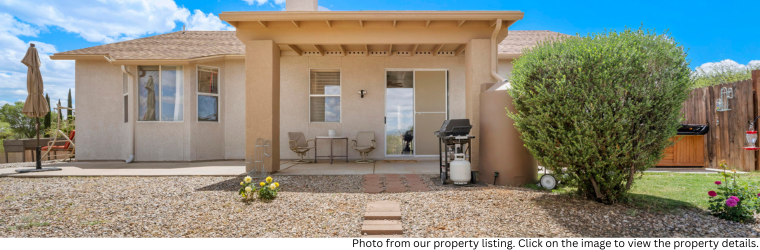 Tidy back yard view with grill, and outdoor patio set on porch. Home exterior features neutral tan and creme colors.