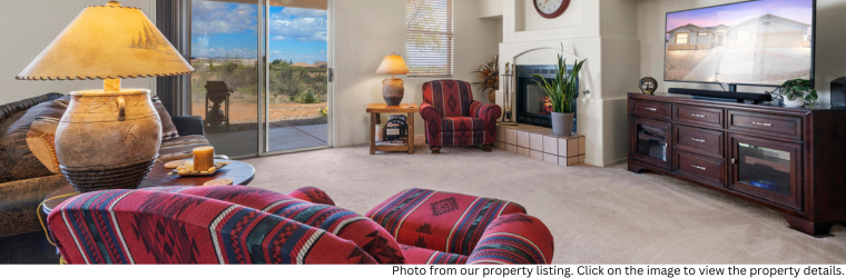 Well-lit living room with couches, tables with table lamps, free-standing entertainment center next to a fireplace. 